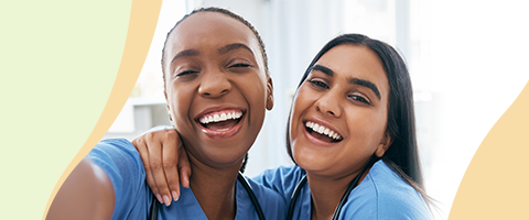 Two smiling nurses in scrubs with arms around shoulders