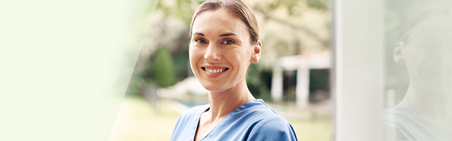 Woman outdoors wearing blue scrubs smiling at camera